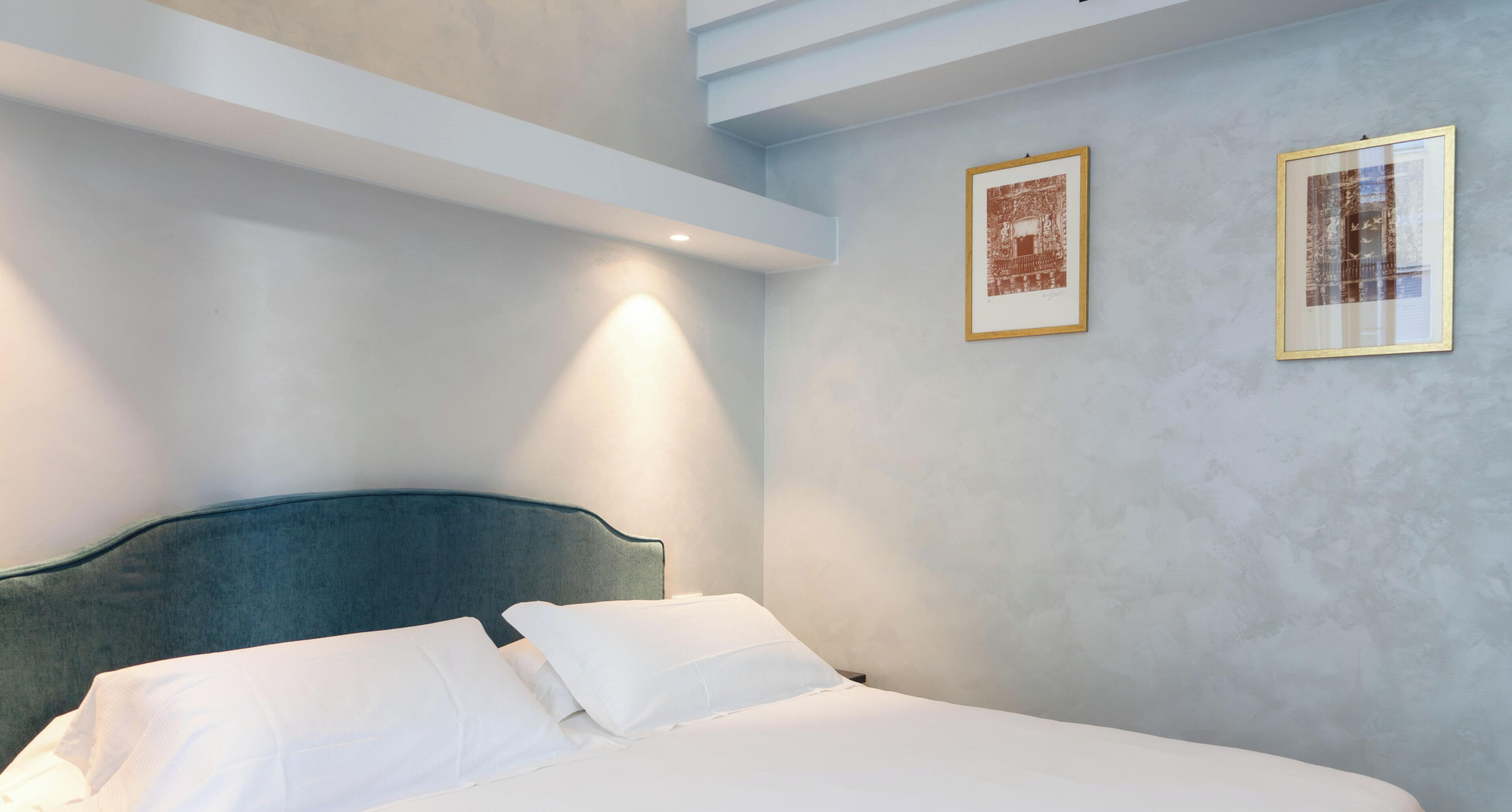 Une chambre à coucher avec un lit, deux tableaux encadrés au mur et un luminaire au plafond.