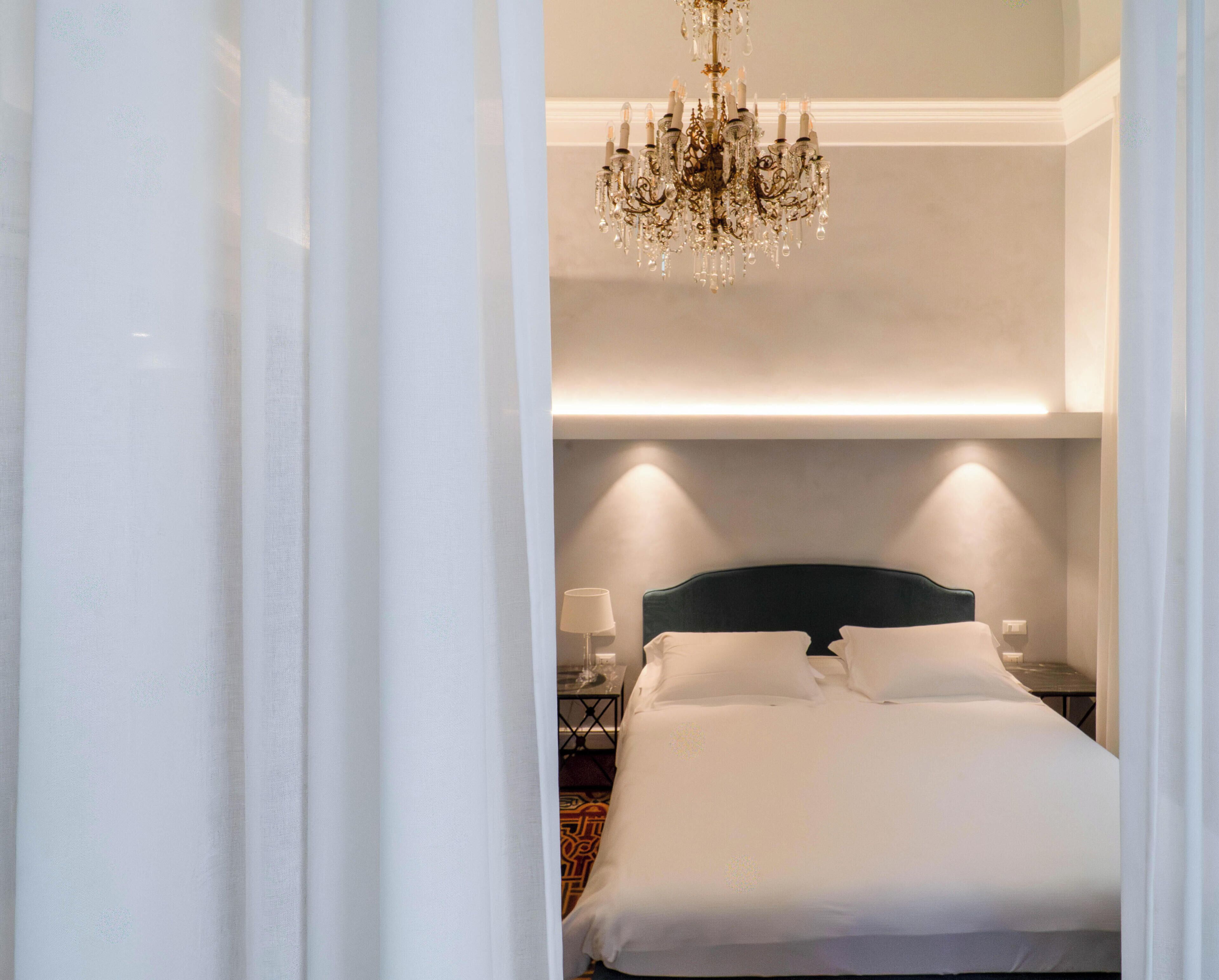 Una habitación de hotel con cama, candelabro, lámparas de noche y mesita de noche.