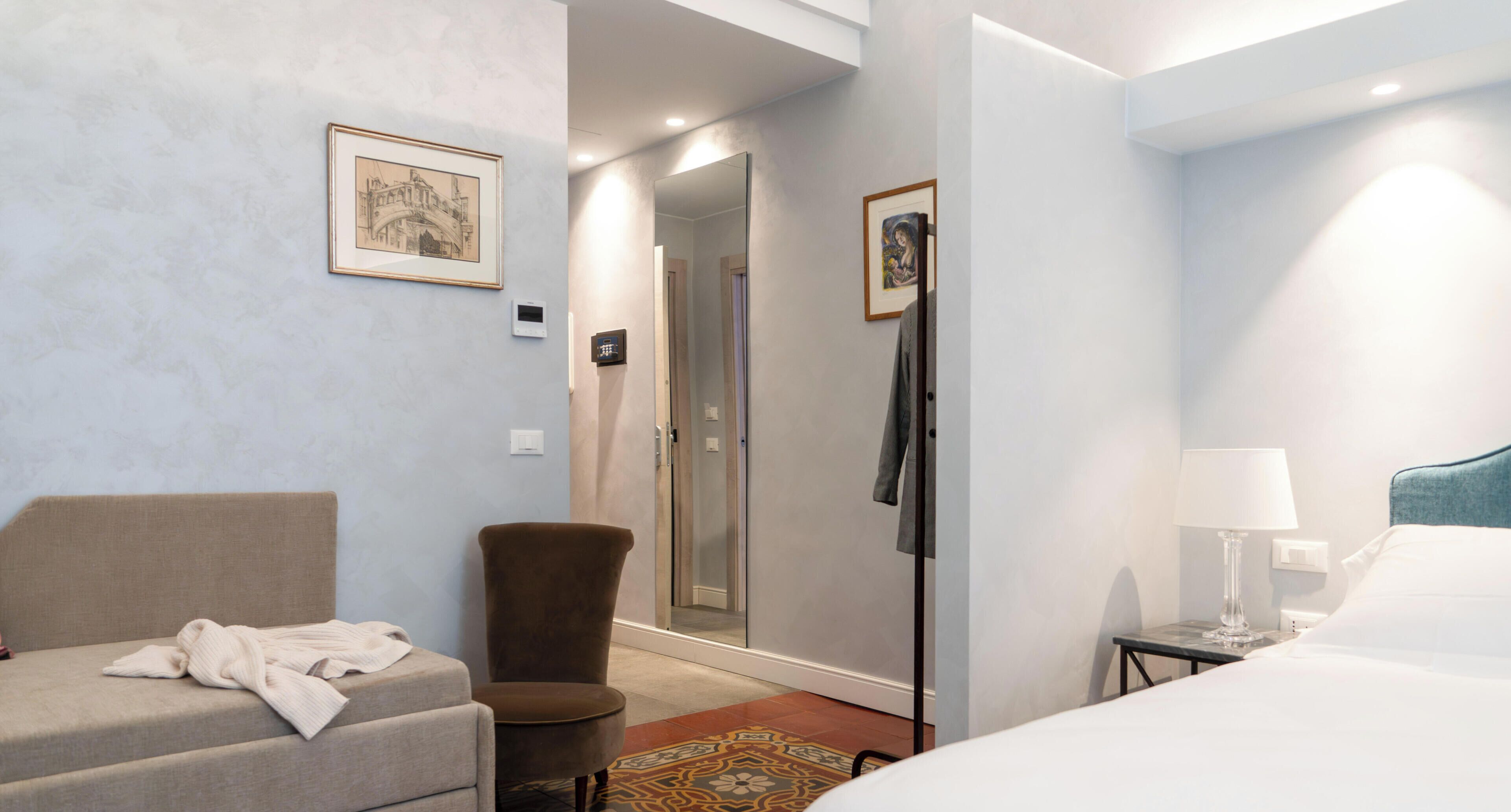 A hotel room with a bed, a chair, a robe, a mirror, and a door leading to a shower.