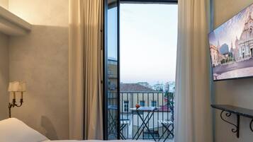 A hotel room with a balcony, a bed, a wall-mounted lamp, and a painting of a building.