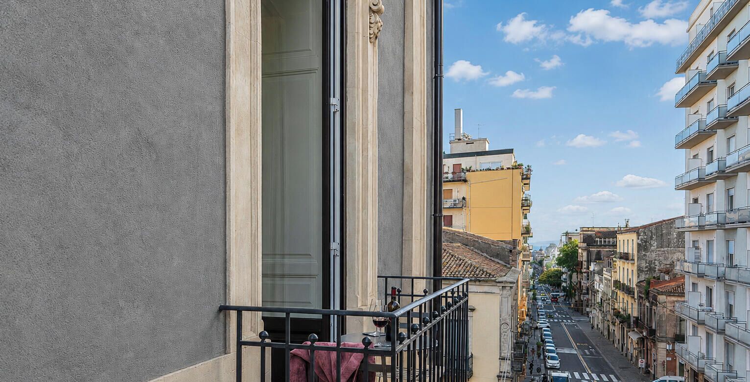 Eine enge Straße mit Häusern an beiden Seiten, ein Balkon mit Geländer und ein klarer Himmel.