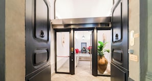 A hotel lobby with a modern design, featuring a central double door, a potted plant, and a staircase leading to the upper floor. - Palazzo Vasta - Charming Rooms (Catania)
