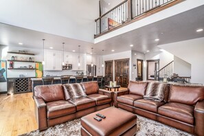 A spacious living area with a brown leather sectional sofa, a coffee table, and a rug. There is a kitchen in the background with white cabinets and a bar area. - Charming 5BR mountain retreat in Deer Valley, Park City, perfect for 14 guests. (Hideout)