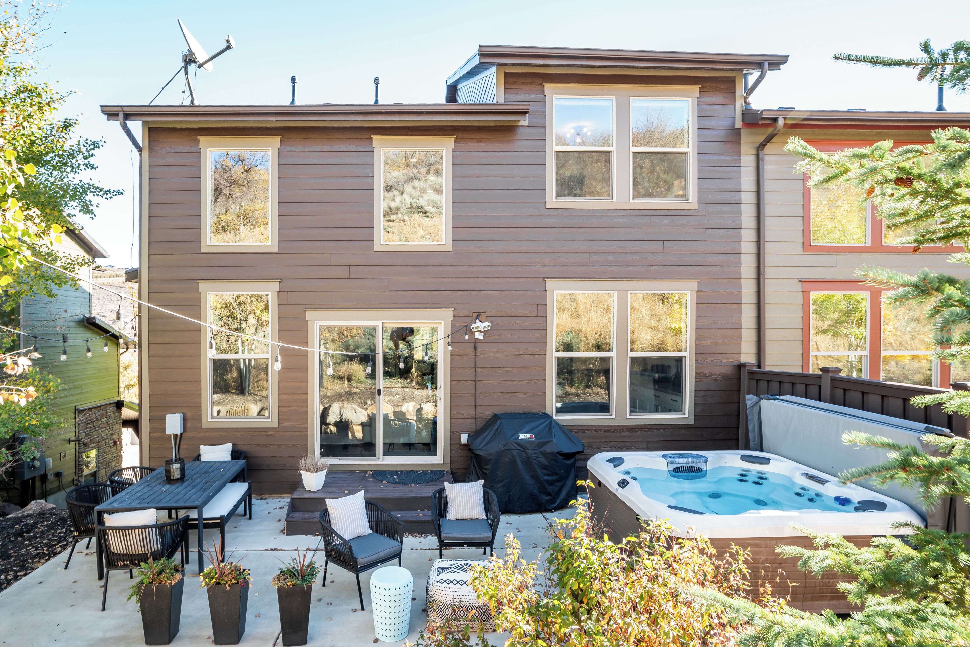 Ein zweistöckiges Haus mit einer Terrassenanlage, die Gartenmöbel, ein Whirlpool und einen überdachten Grillplatz bietet.