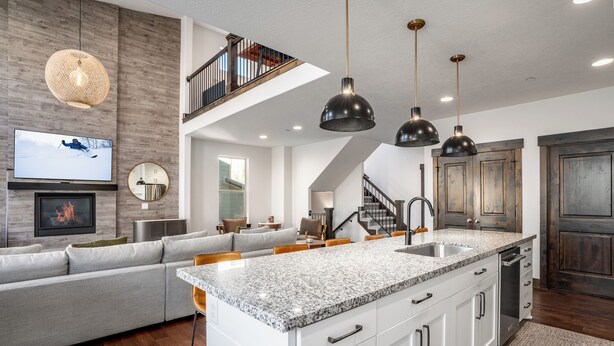 A modern kitchen with a large island, white cabinetry, and a dining area with a gray sofa and wooden chairs. - Luxurious 4-bedroom retreat in Deer Valley, Park City, with hot tub (Hideout)
