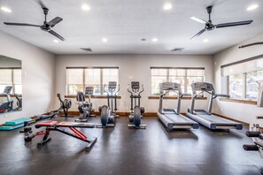 Et fitnessrum med loftsvifte, løbebånd, crosstrainere og vægtbænke.
