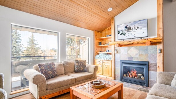 Ein gemütliches Wohnzimmer mit Kamin, Holzbalkendecke und großen Fenstern.