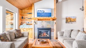 Ein gemütliches Wohnzimmer mit Kamin, einem an einem Holzbalken befestigten Fernseher und einer Couch.