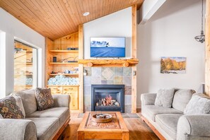 Ein gemütliches Wohnzimmer mit Kamin, einem an einem Holzbalken befestigten Fernseher und einer Couch.