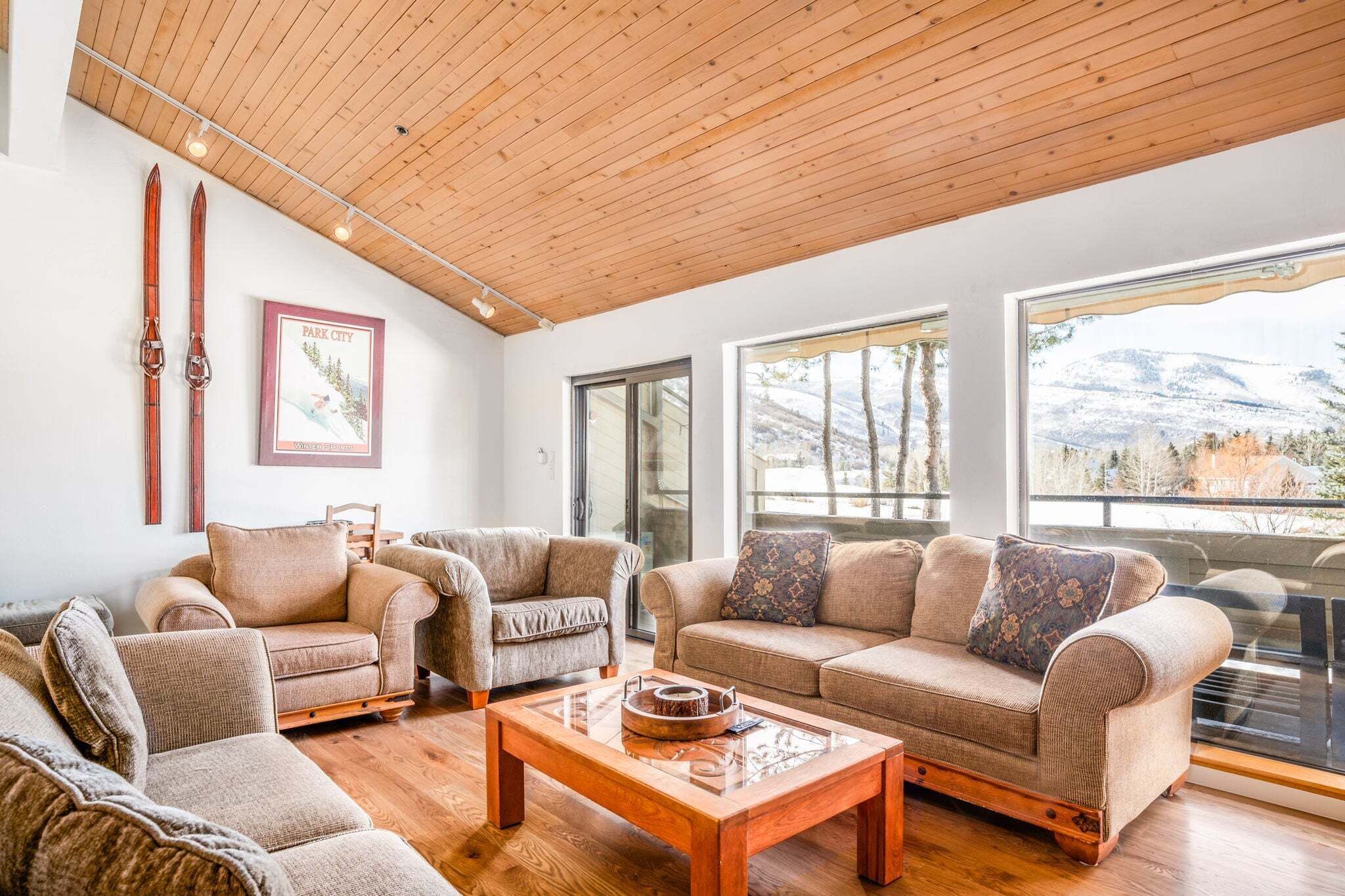 Un vaste salon doté d’un plancher en bois, d’un plafond en bois et de grandes fenêtres offrant une vue sur les montagnes.