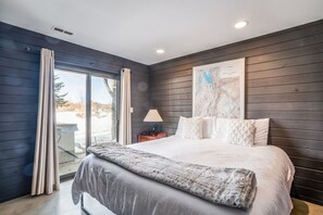 Ein Schlafzimmer mit einem großen Bett, einem Nachttisch, einer Lampe, einer Karte an der Wand und einer Glastür zum Außenbereich.