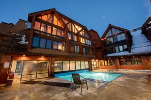 A two-story building with a swimming pool, large windows, and a covered outdoor area. - Ski-In/Out Base Village | 3BR w/ Pool, Gym & Hot Tub (Park City)