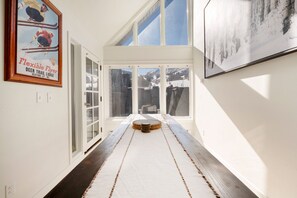 A hallway with a rug leading to a door, framed pictures on the walls, and a view of a snowy landscape through large windows. - Ski-In/Out Base Village | 3BR w/ Pool, Gym & Hot Tub (Park City)