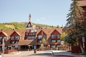 A building with a prominent tower and multiple windows, surrounded by a hilly landscape. - Ski-In/Out Base Village | 3BR w/ Pool, Gym & Hot Tub (Park City)