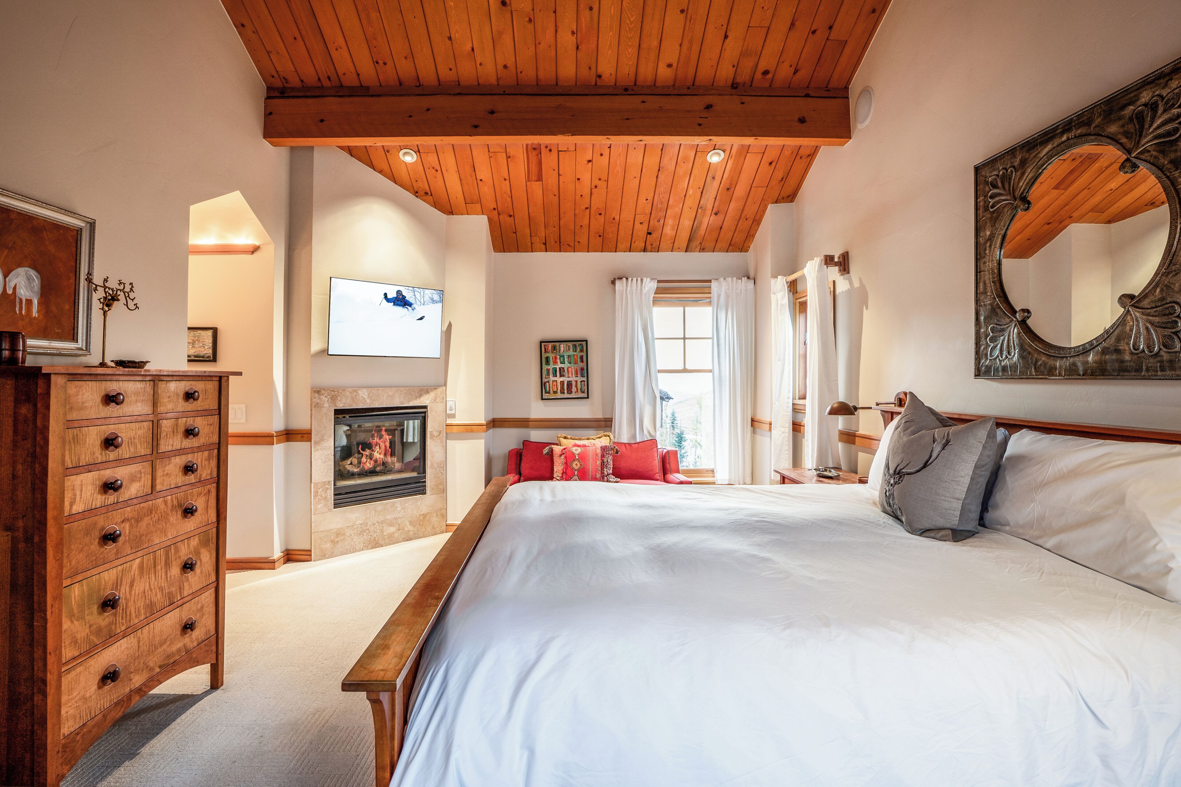 Ein Schlafzimmer mit Holzboden, Kamin, einem Bett mit weißer Bettwäsche, einem Schminktisch und einem großen Spiegel.