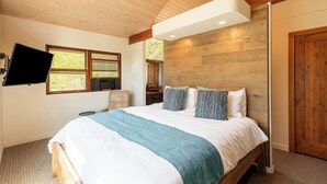 Een slaapkamer met een bed, een wandtelevisie, een houten plafond en een raam.