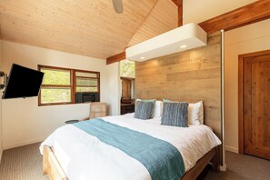 Una camera da letto con un letto, una televisione a parete, soffitto in legno e una finestra.