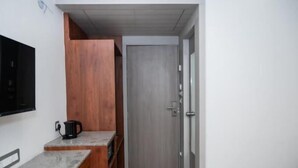Ein kleines Zimmer mit Küchenzeile, einem Holzschrank, einer Tür und einem an der Wand befestigten Fernseher.