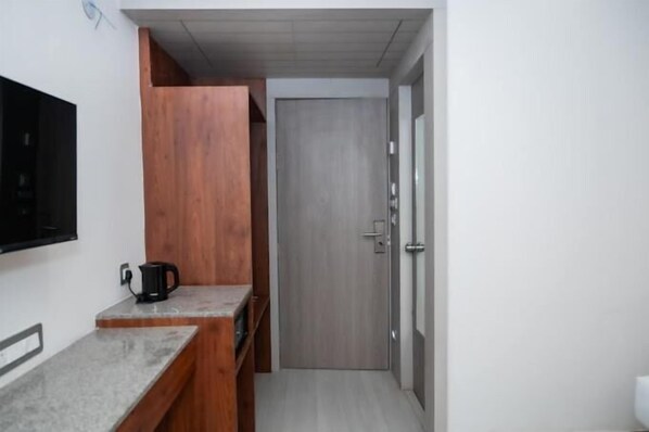 A compact room with a kitchenette, a wooden cabinet, a door, and a wall-mounted TV.