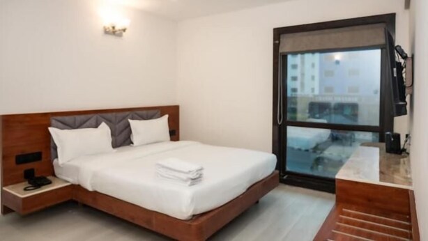 Ein modernes Hotelzimmer mit einem hölzernen Bett, einem Nachttisch mit Telefon, einem großen Fenster mit Blick und einem Flachbildfernseher.