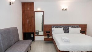 Ein Schlafzimmer mit einem Bett, einem grauen Sofa, einem Holzschrank und einem Spiegel.