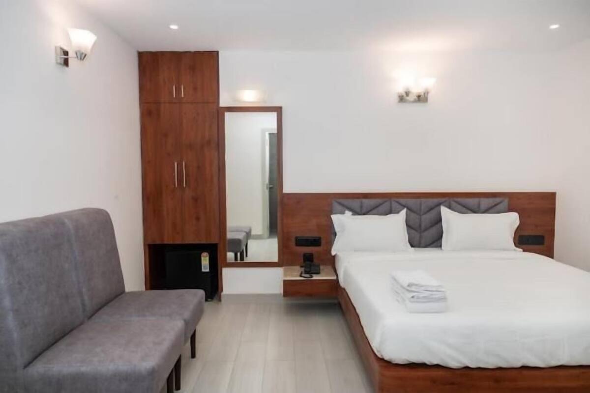 Un dormitorio con una cama, un sofá gris, un armario de madera y un espejo.