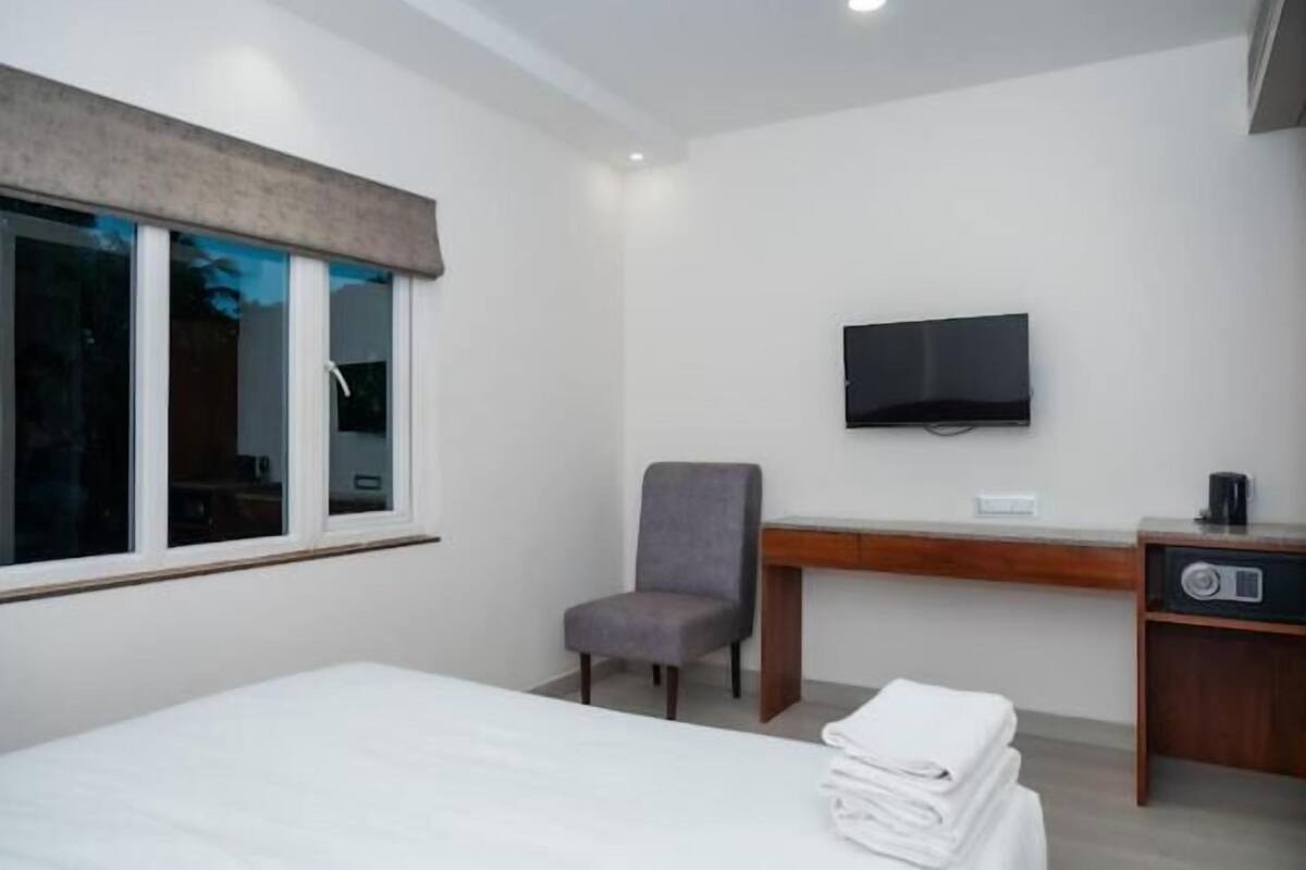 Una habitación de hotel con cama, escritorio, silla, televisor y cafetera.