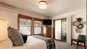 Un dormitorio con cama, cómoda, televisor y vistas al exterior.