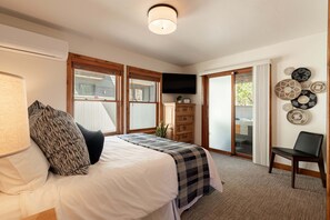 Ein Schlafzimmer mit Bett, Kommode, Fernseher und Blick ins Freie.