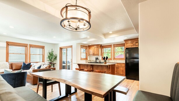 Un amplio salón con un gran comedor de madera, una cocina con armarios de madera y un refrigerador negro.