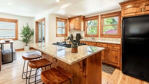 Una cocina con armarios de madera, un refrigerador negro, encimera de granito y una planta en maceta.