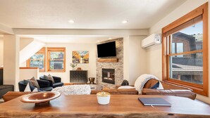 Una sala de estar moderna con chimenea de piedra, un televisor de pantalla plana y un gran comedor de madera.