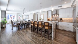 A modern kitchen with a central island, bar stools, and a dining area with a large window. - Steps from Town Lift & Main Street! Luxe amenities! (Park City)