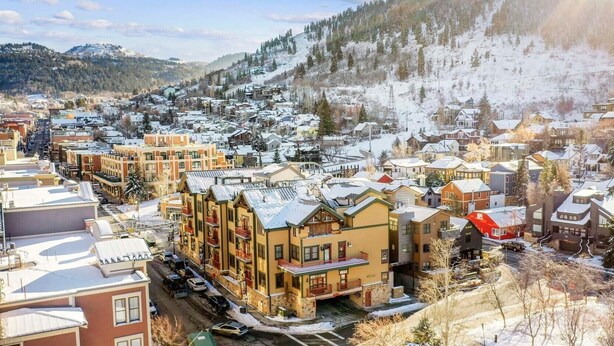 A snow-covered town with a mix of residential buildings, including a prominent multi-story hotel with balconies and a ski resort in the background. - Steps from Town Lift & Main Street! Luxe amenities! (Park City)