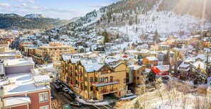 Une ville enneigée, avec un mélange de bâtiments résidentiels, dont un grand hôtel à plusieurs étages doté de balcons, et une station de ski en arrière-plan.