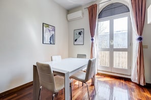 Ein Essbereich mit einem weißen Tisch, vier Stühlen, einem Fenster mit Vorhängen und zwei gerahmten Bildern an der Wand.