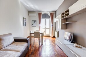 Ein modernes Wohnzimmer mit einer Couch, einem Esstisch, Stühlen, einem Fernseher und Einbauschränken.