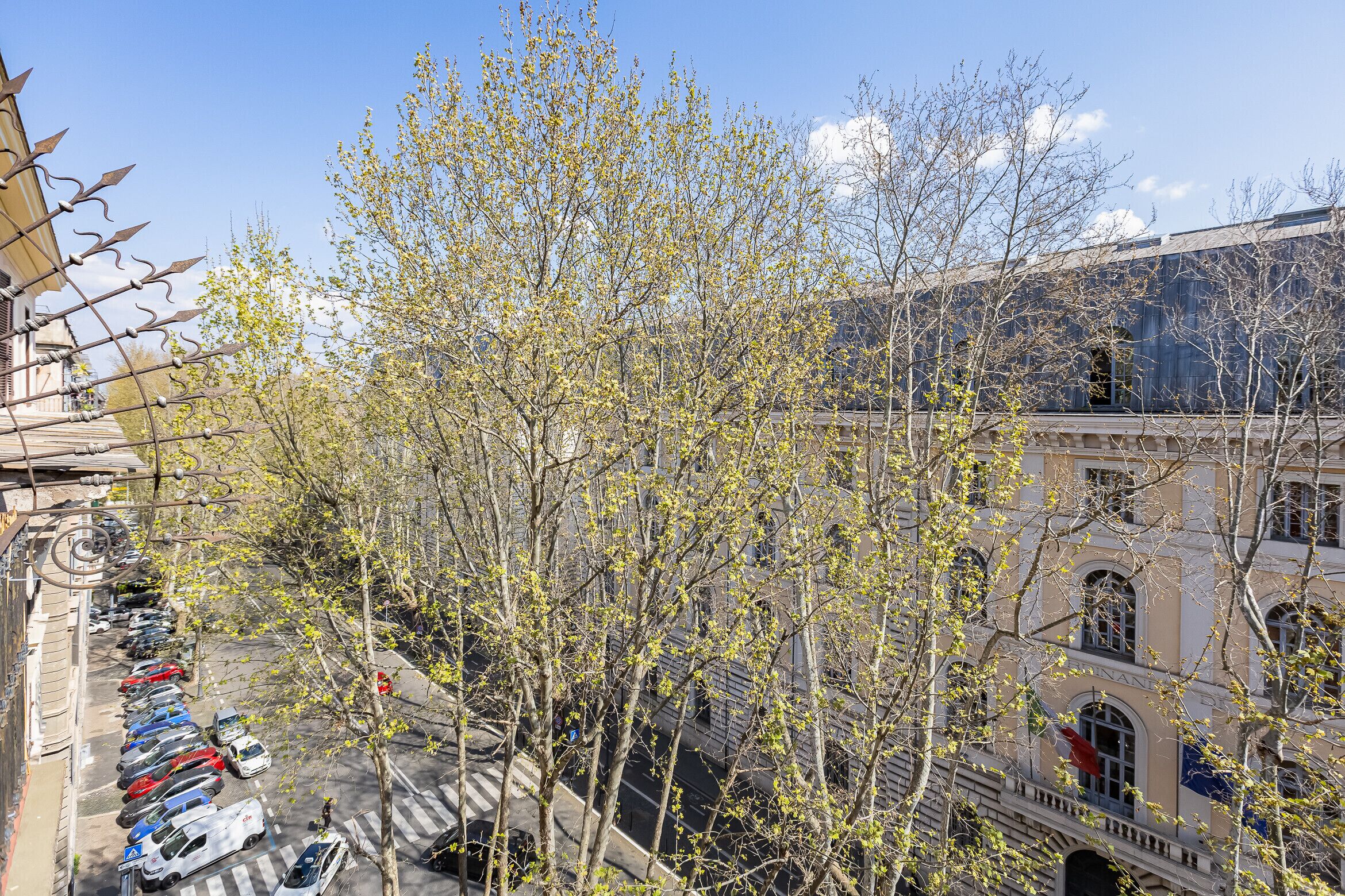 A building with a row of parked cars and trees in front.