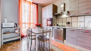 Eine moderne Küche mit Essbereich, Edelstahlgeräten und einem Fenster mit orangefarbenen Vorhängen.