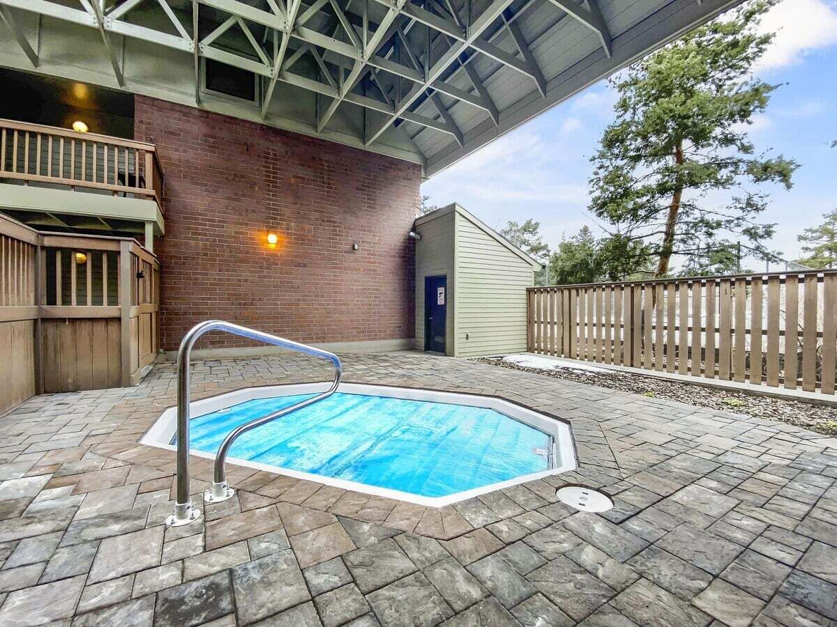 A swimming pool with a metal ladder, surrounded by a brick wall and a wooden fence.