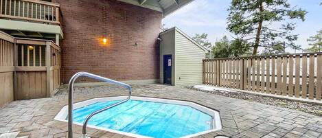 A swimming pool with a metal ladder, surrounded by a brick wall and a wooden fence.