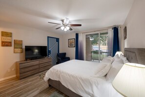 Ein Schlafzimmer mit Bett, Fernseher, Deckenventilator, Kommode und einem Fenster mit Vorhängen.