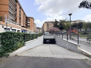 Ein gepflasterter Weg führt zu einem verschlossenen Eingangstor, umgeben von Wohngebäuden und einem Park mit Spielgeräten.
