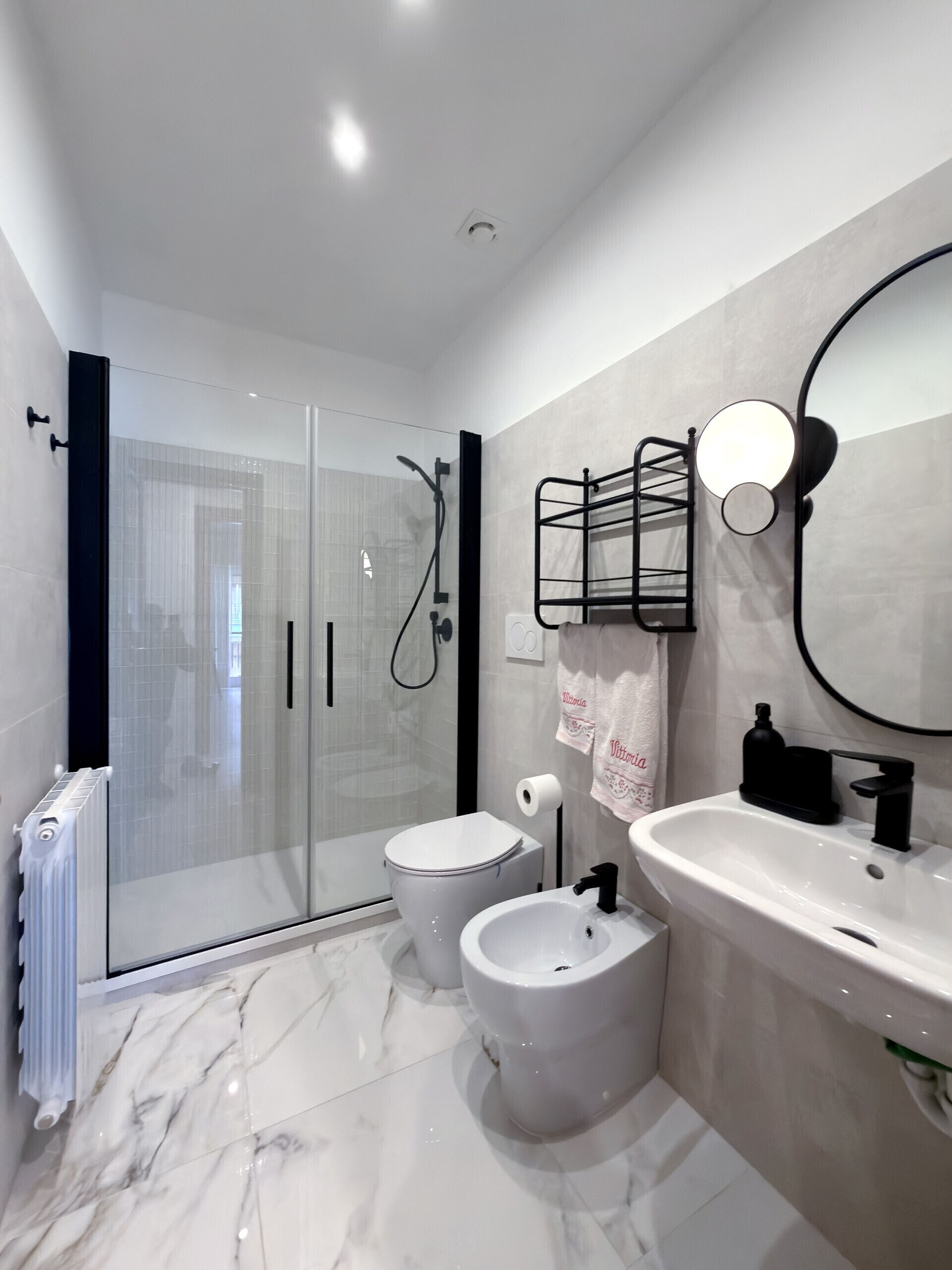 Een moderne badkamer met een douchecabine van glas, een toilet, een bidet en een wastafel met spiegel.
