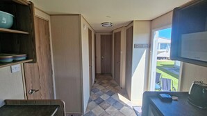 Un pasillo estrecho con armarios de madera, suelo de baldosas y una ventana que da a una casa.
