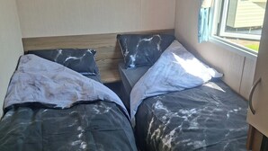 Habitación pequeña con dos camas, una ventana con cortinas y un cabecero de madera.
