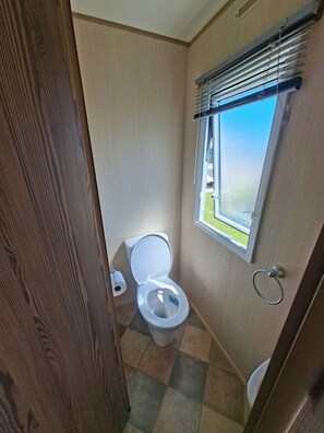 A small bathroom with a toilet, a window, and a towel ring. - Highfields Skegness Cabin Near Beach & Pier (Skegness)