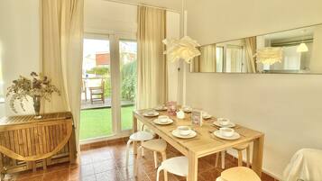 A dining area with a wooden table set for four, a vase with flowers, and a view of the outdoors.