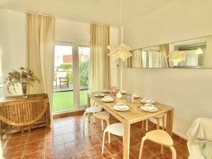 Un comedor con una mesa de madera dispuesta para cuatro personas, un florero con flores y vistas al exterior.