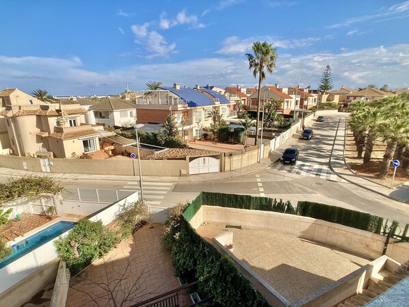 A residential street with houses, a swimming pool, and a clear sky.